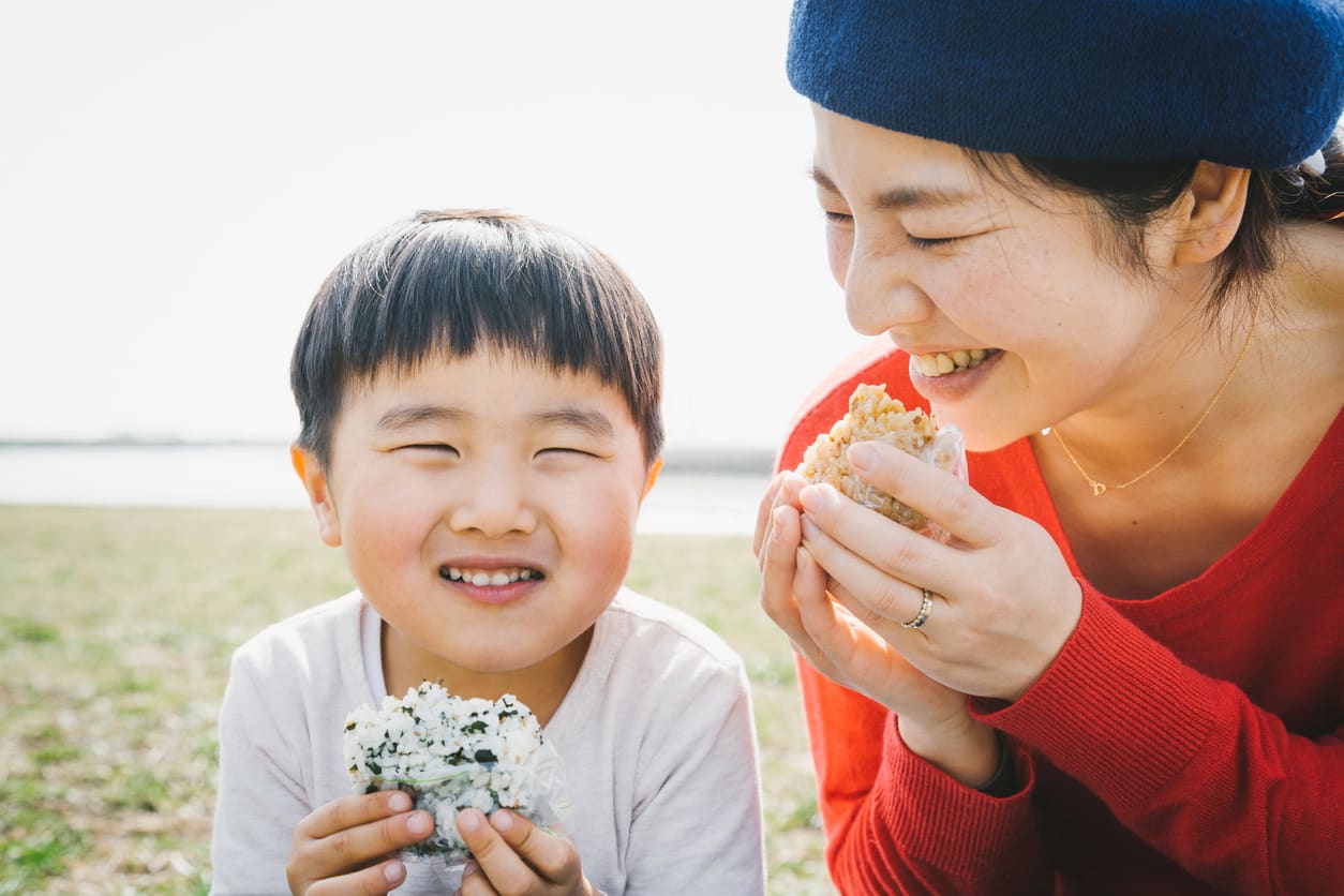 田んぼのそばでおにぎりを食べる親子(イメージ写真)
